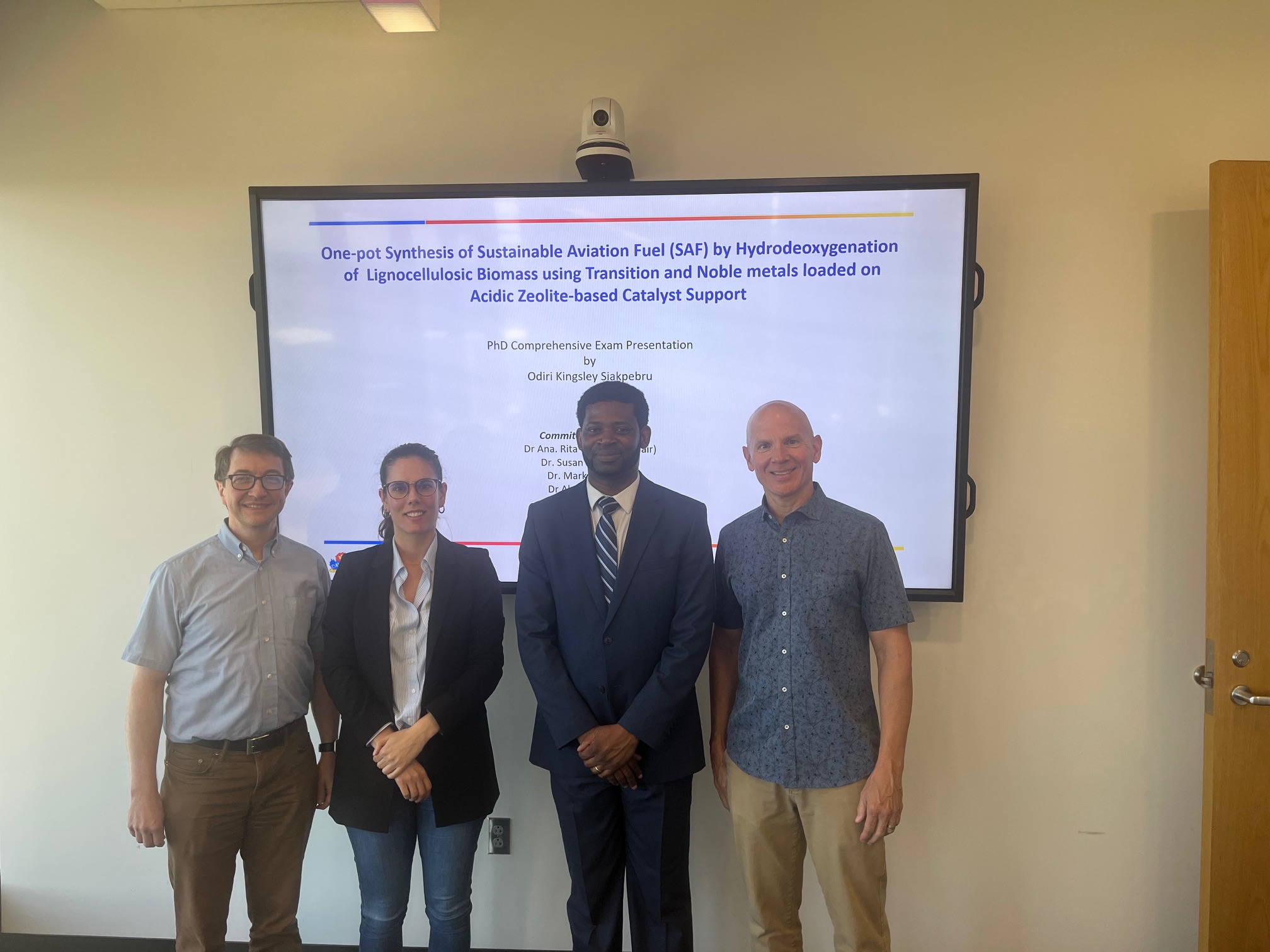 Four people stand in front of a large television screen