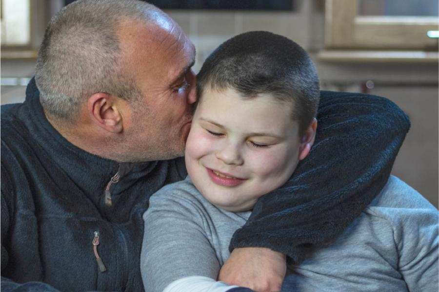 A father hugs his school-aged son who is smiling while they sit together