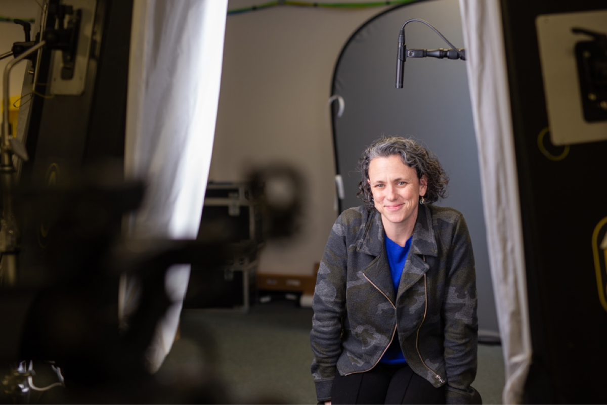 Interviewee smiles with audio and lighting equipment surrounding her. 