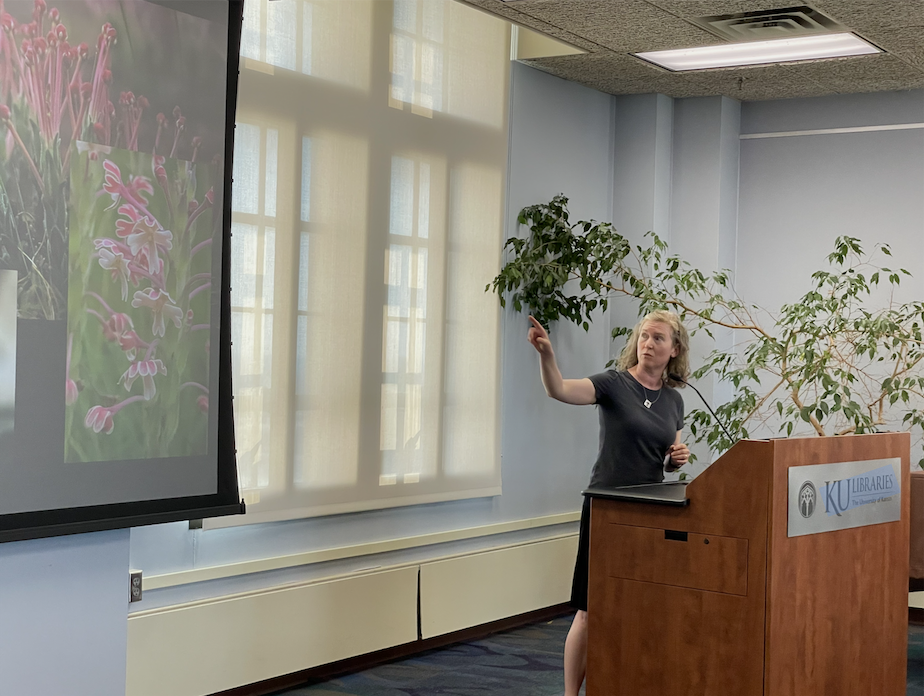 Woman with blond curly hair gestures to screen with flowers