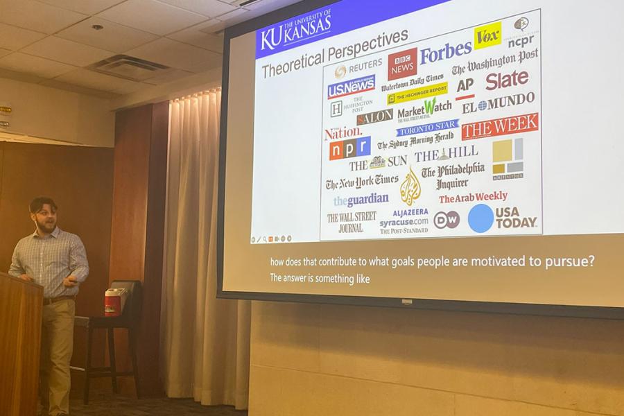 Logan Edmondson at podium with overhead presentation showing logos for companies for many media companies including AP, Slate, Marketwatch, NPR, The Nation and more.