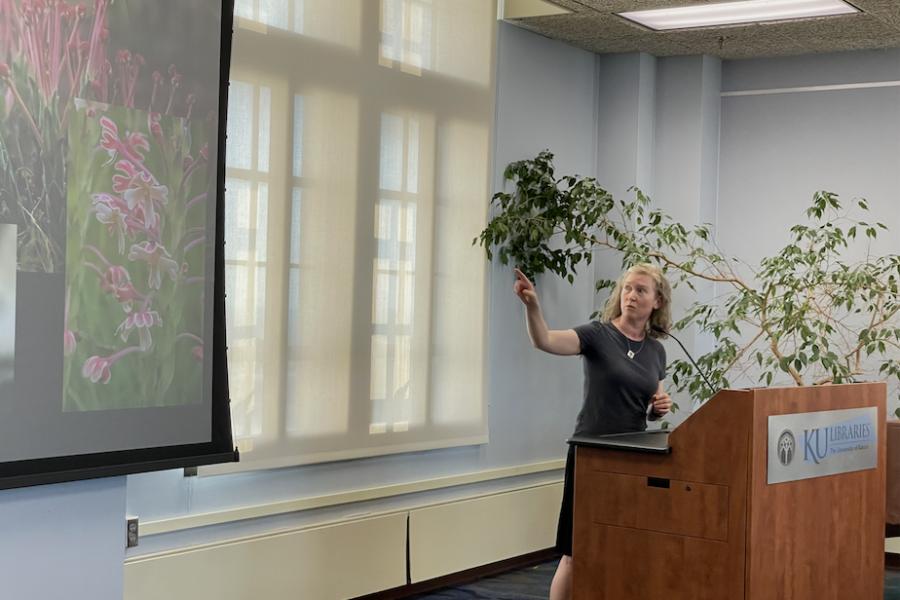 Woman with blond curly hair gestures to screen with flowers