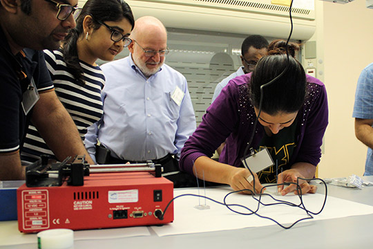 Mahsa epoxies her chip while Md Foysal, Kavya, and Prof. Kaufman watch.