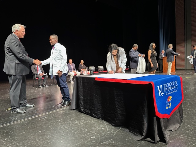 Ronald Ragan, dean of the School of Pharmacy, congratulates student Kossivi Abalo while student Haya Abbas signs the Pledge of Professionalism at the school's 2023 white coat ceremony.