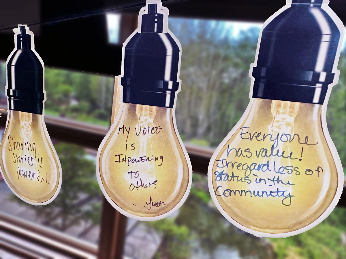 Pieces of paper in the shape of lightbulbs with messages written on them in pen. Sharing stories is powerful. My voice is empowering to others. Everyone has value. Regardless of status in the community.