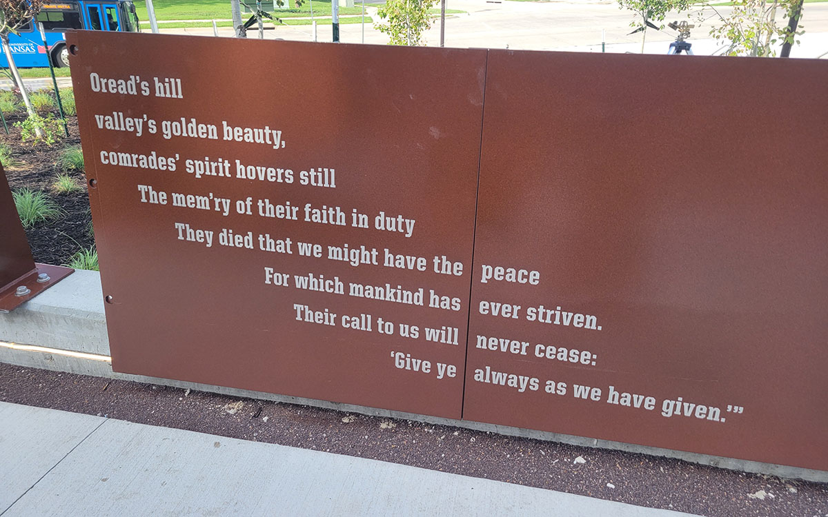 Aluminum plaque outside David Booth Kansas Memorial Stadium commemorating Jayhawks who lost their lives in World War I. The inscription includes KU's memorial hymn.