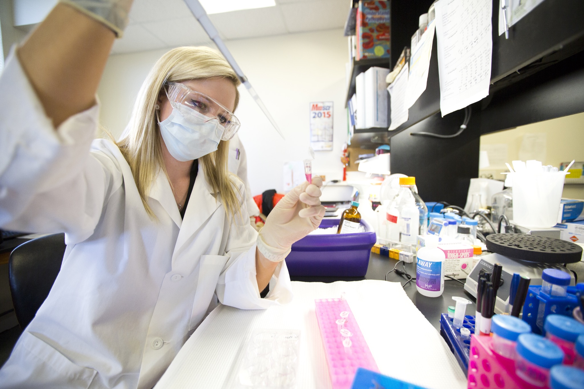 Masked student in lab coat works with sample in lab