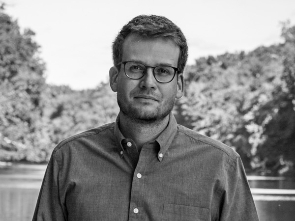 John Green stands in front of a tree-lined lake.