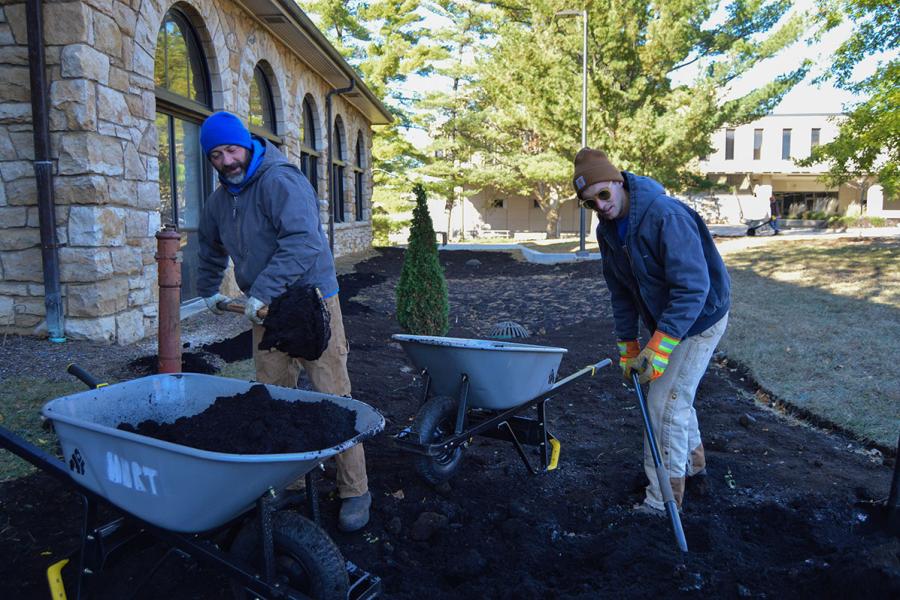 Scott Cramer and Willie Justus, landscape workers, shovel mulch into wheelbarrows during a bed renovation outside of Stauffer-Flint Hall in November 2023.