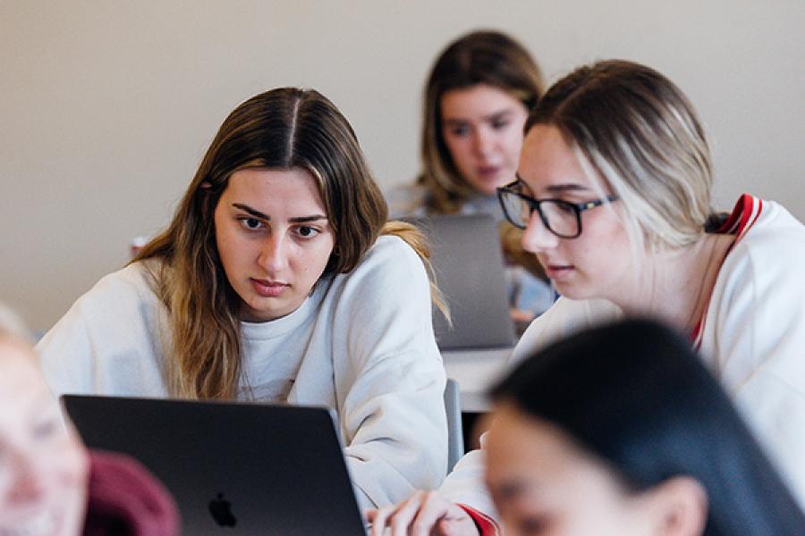Group of students concentrated on working together with laptops, in a classroom setting.