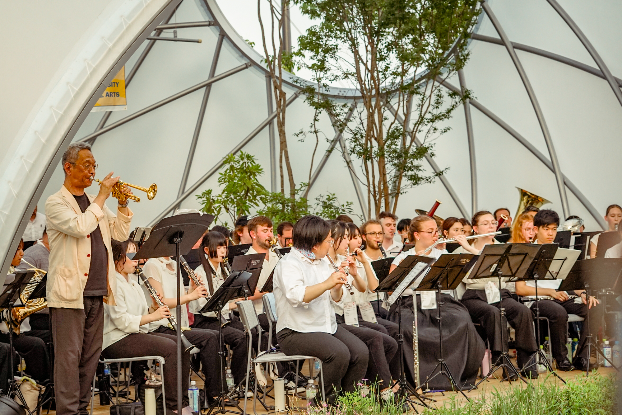 a group of musicians playing wind instruments seated and playing at an outdoor bubble stage venue