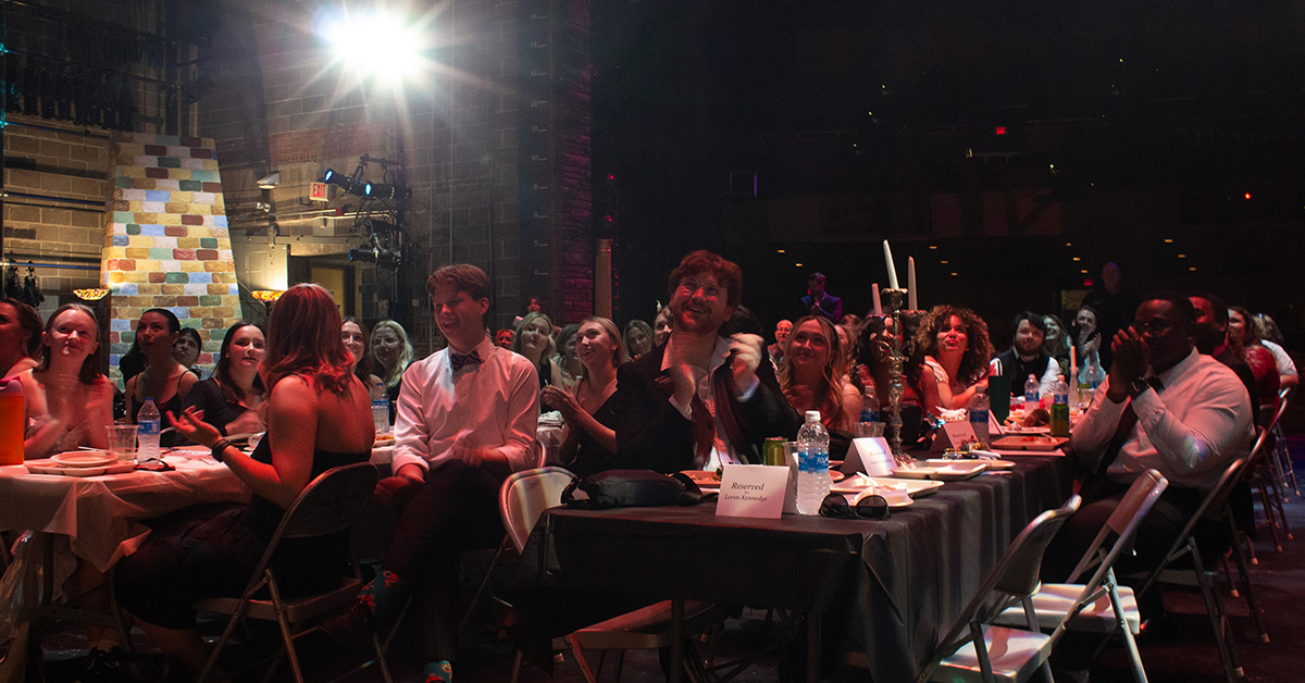 Group of dressed up students seated at a table and clapping