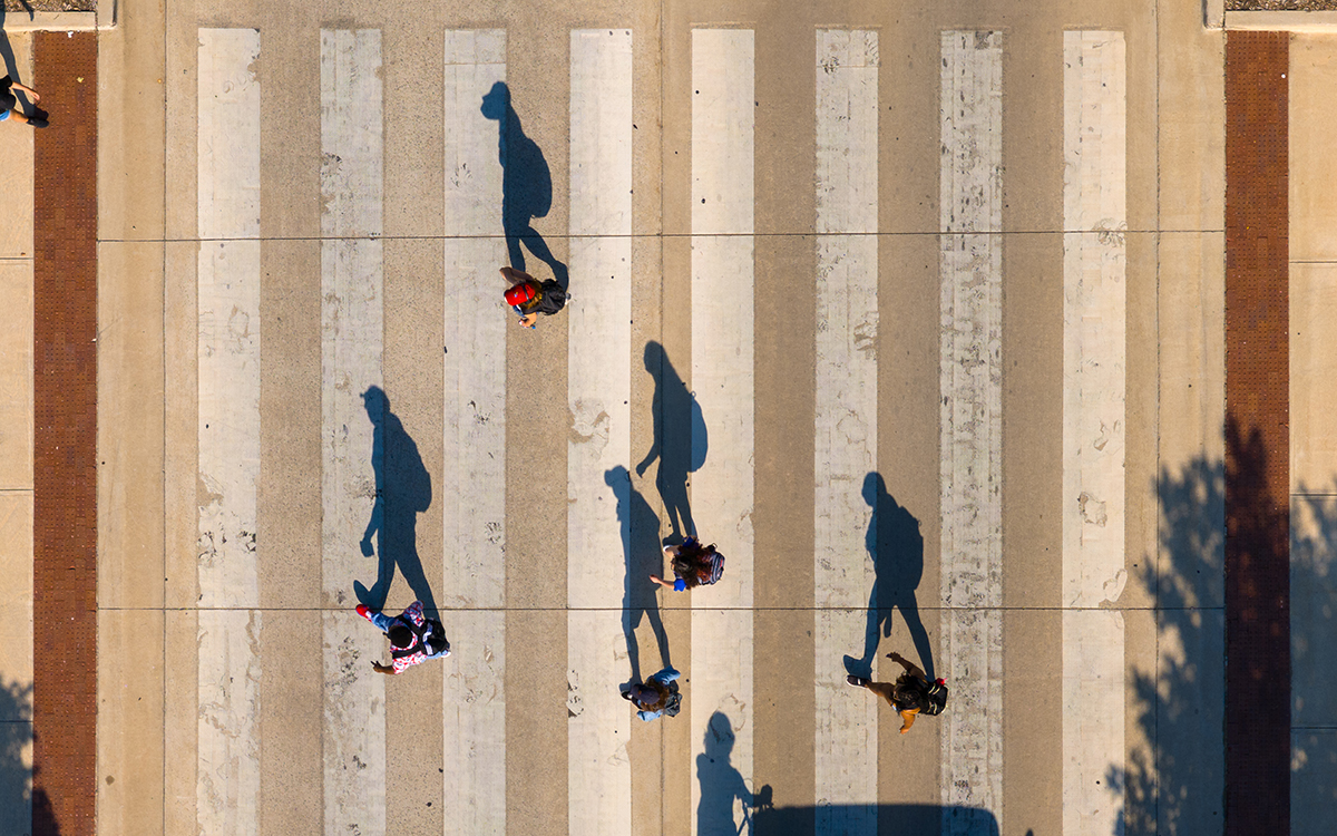 Students on crosswalk on Jayhawk Boulevard, casting shadows in late afternoon sun.