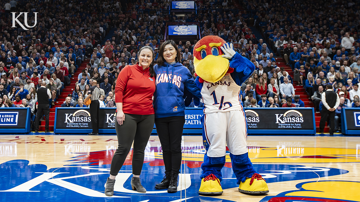 Hui Cai, chair and professor of architecture, center, was recognized for research excellence during the Dec. 22, 2023, KU men’s basketball game at Allen Fieldhouse. She is pictured on the court with Belinda Sturm, interim vice chancellor for research, and KU mascot Baby Jay.