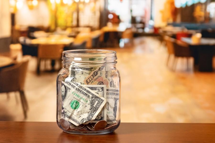A Mason jar filled with tips sits on a counter of a restaurant.