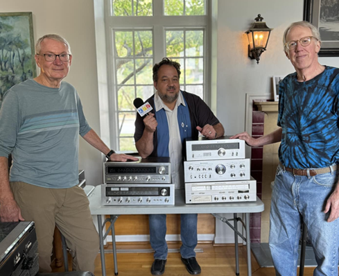 Sale volunteers Ed and Douglas with KPR Morning Host J Schaefer in front of a table holding stereo equipment.