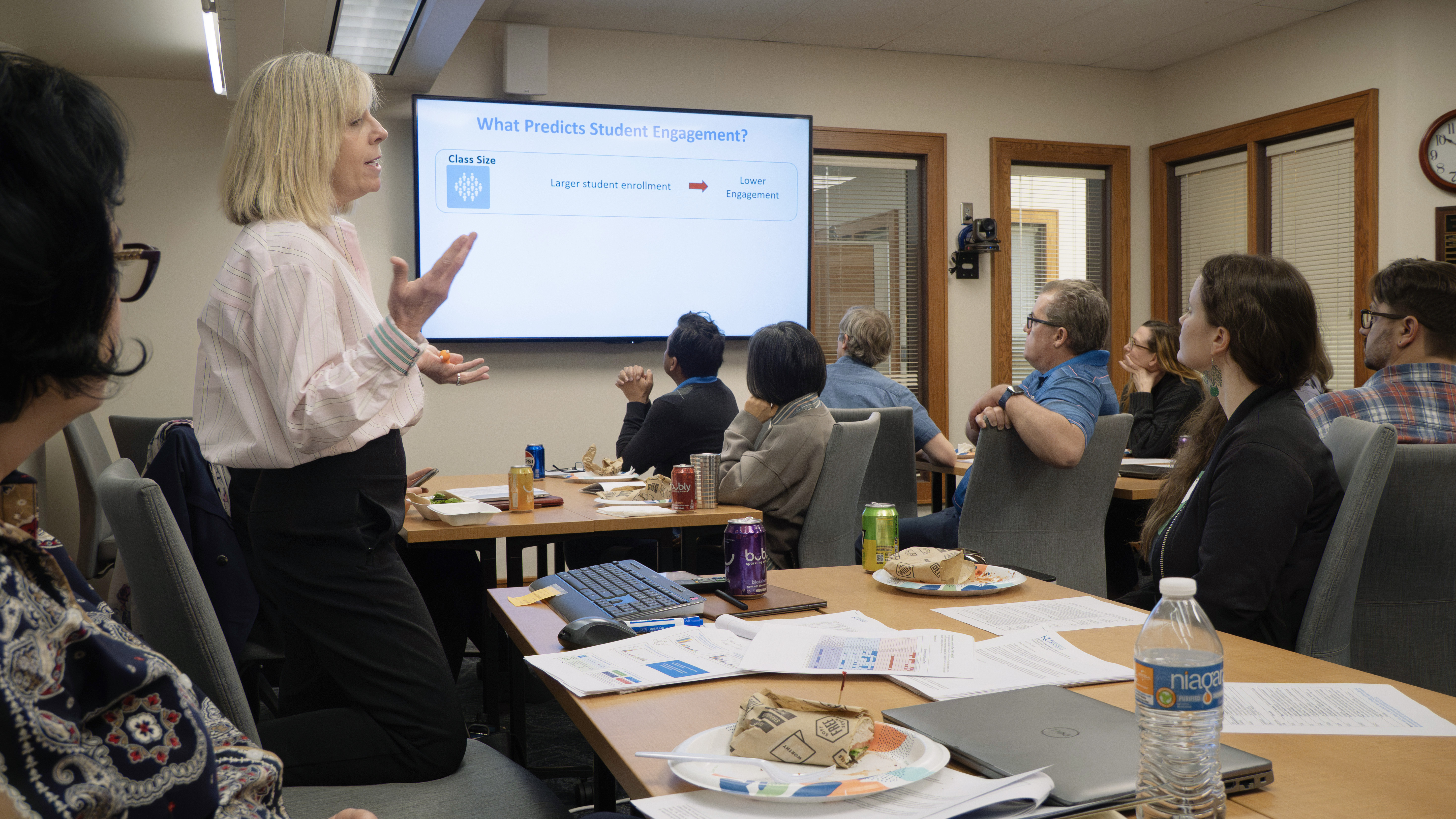Woman speaks to a conference room full of people who are looking at a large television