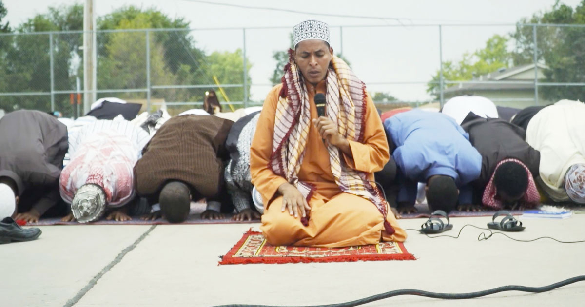 person kneeling in prayer mat in front of others bowed and praying
