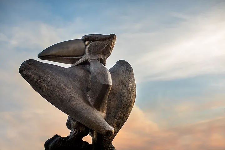 A bronze Jayhawk statue against a sunset sky.