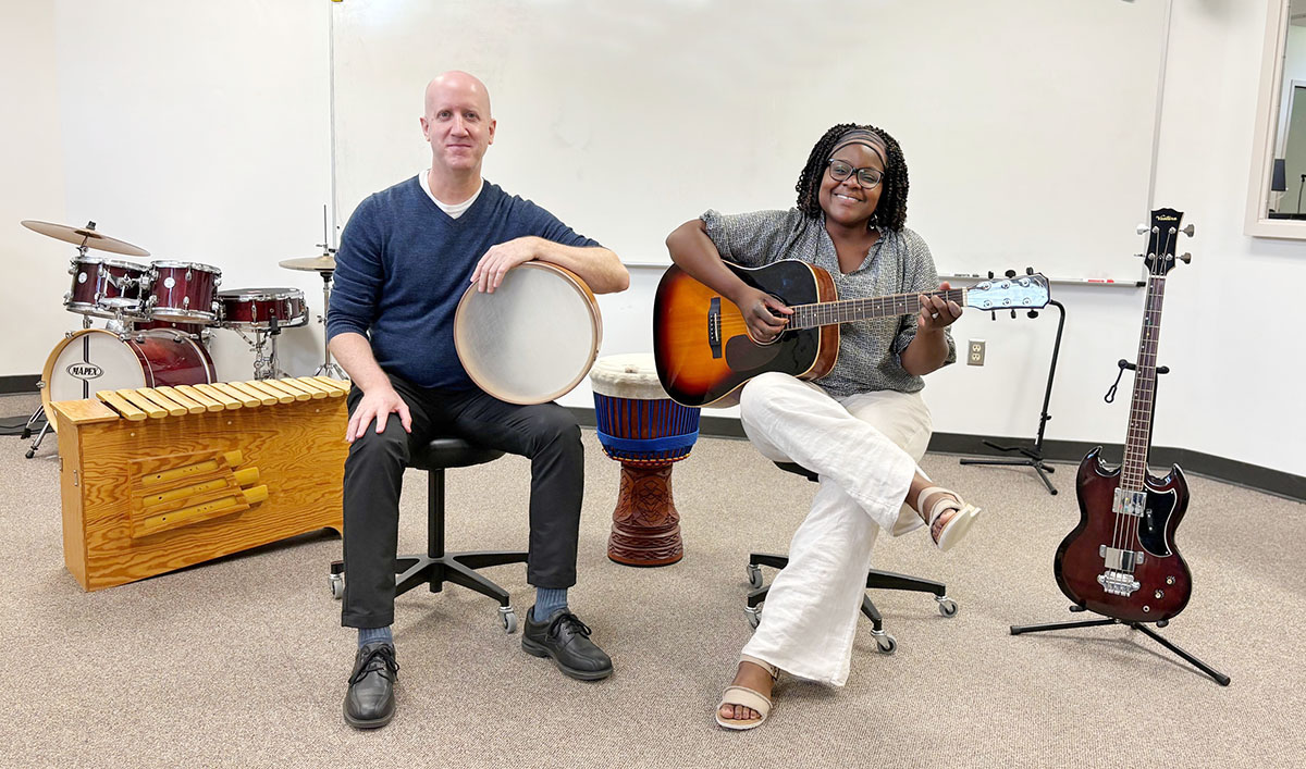 Man, seated, holding drum. Woman, seated, holding guitar. Other instruments around.