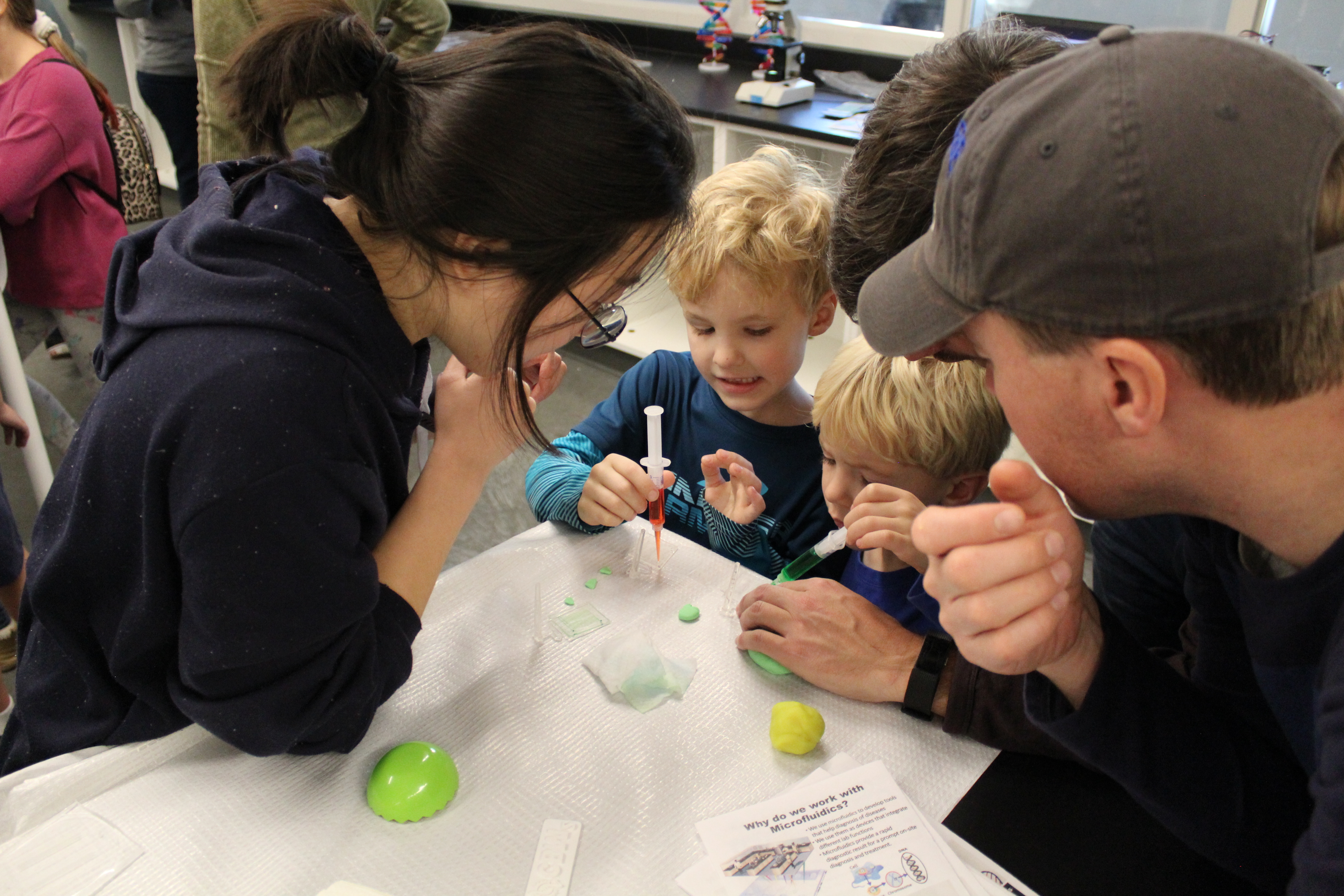 A family of children pouring a colored substance into a glass.