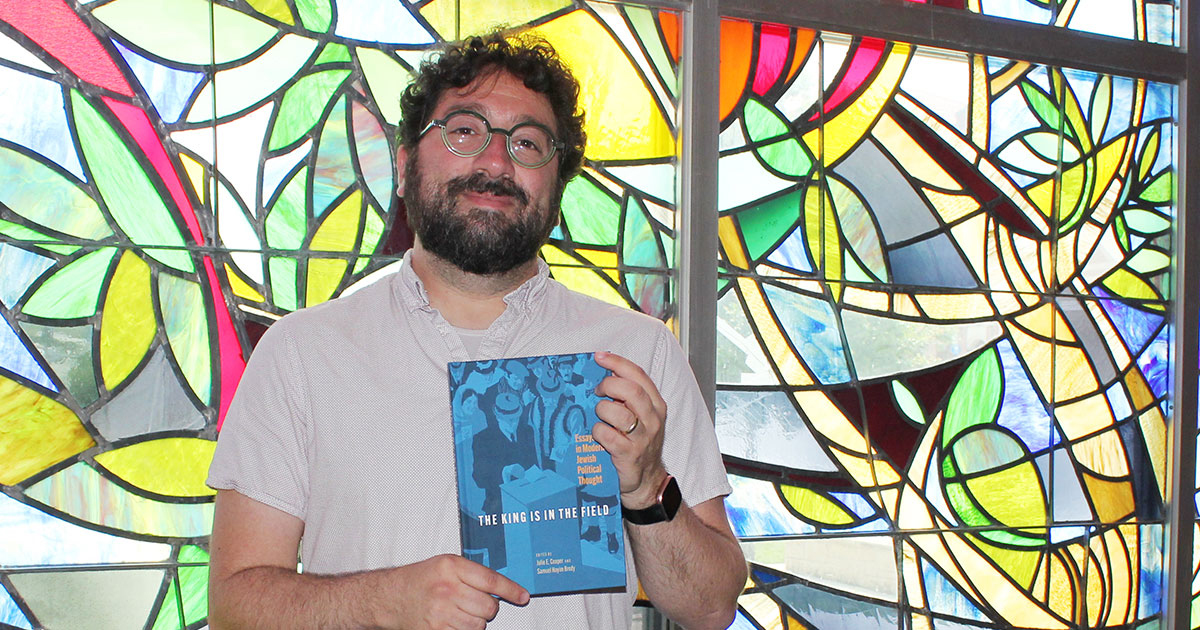 Image: Samuel Brody in Smith Hall with a copy of the book he co-edited, “The King is in the Field: Essays in Modern Jewish Political Thought.” Credit: Rick Hellman, KU News Service