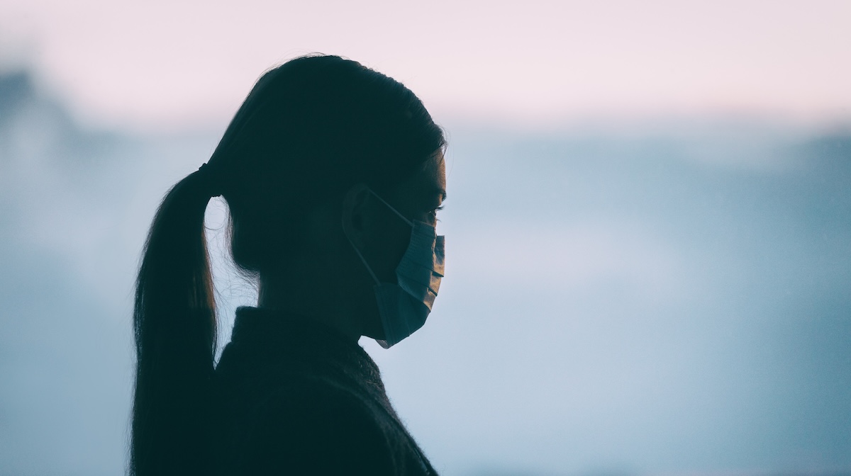 A young Asian woman wears a COVID mask while staring into the distance.