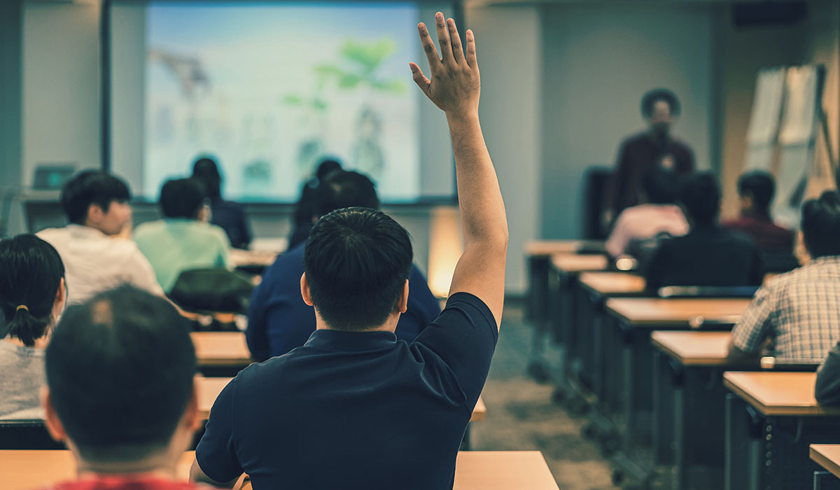 An image of a student raising his hand in class.