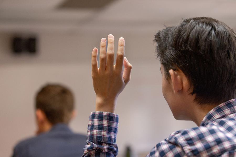 An image of a student raising his hand in a classroom.