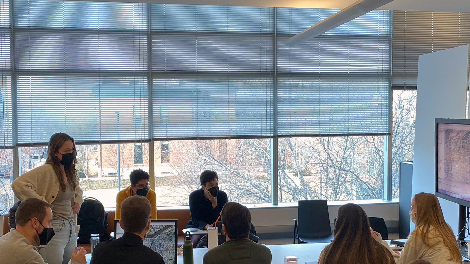 Color photograph shows students discussing architecture studio project around large table.