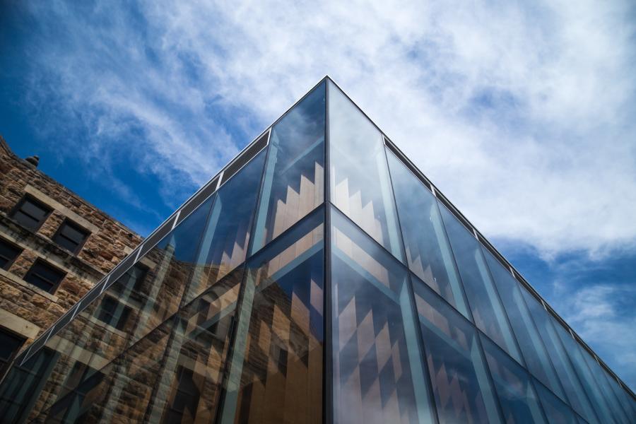 View looking up at the corner of the Marvin Hall Forum's glass exterior facade against a blue sky and scattered white clouds.