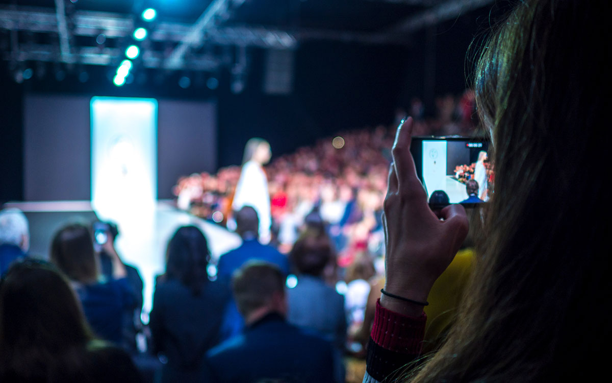 Woman holding camera recording fashion show with model on runway