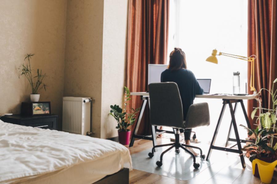 A woman on her computer from a desk inside her bedroom.