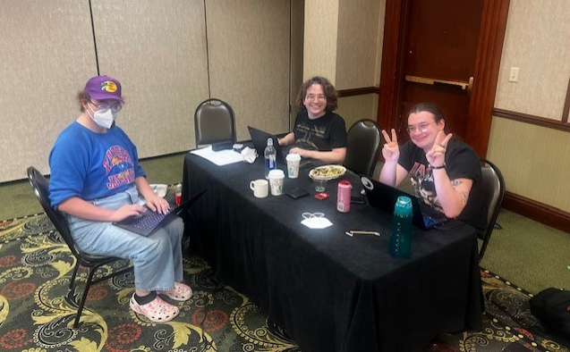 Assistant Coach Ryan Cavanaugh with Luna Schultz and Rose Larson, all seated in hotel conference room space.
