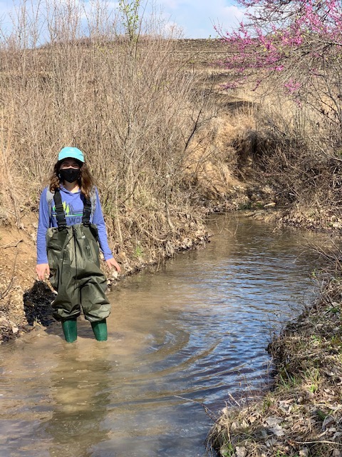 Eva standing in a stream surrounded by prairie grasses