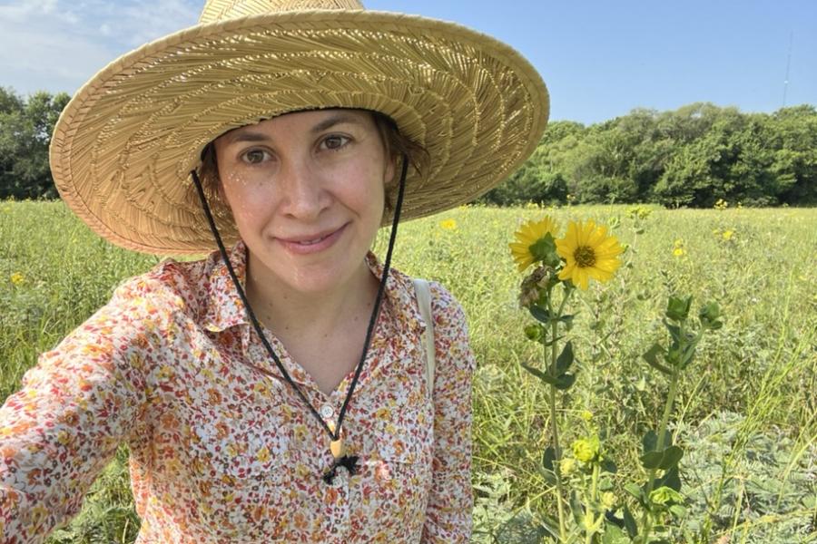 Young person wearing straw hat and floral shirt, standing in a field looking at camera.