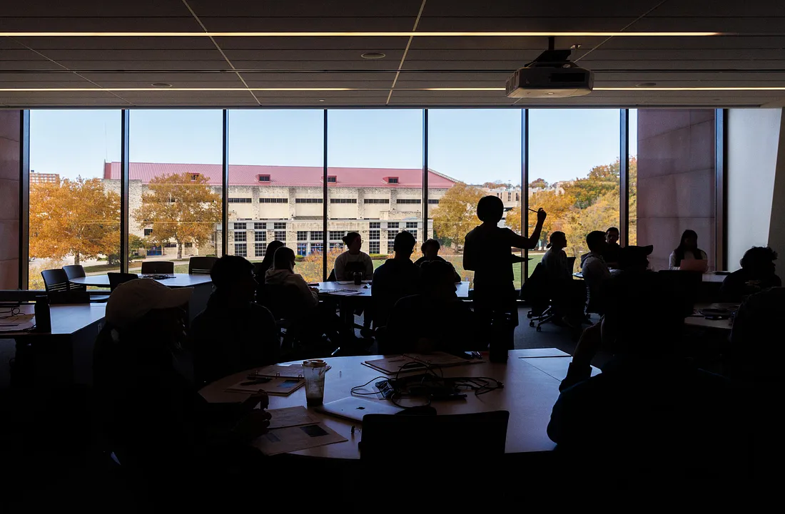 A professor teaches in a classroom overlooking Allen Fieldhouse.