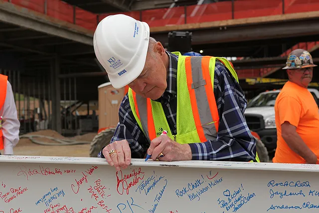 A man in a hard hat and high-visibility vest signing a beam at a construction site.