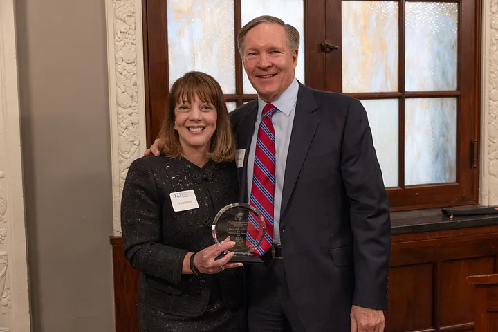A women wearing a black dress presents a glass award to a man in a suit with a red and blue stripped tie.