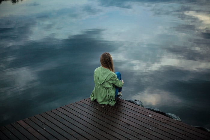 Individual sitting on edge of dock. Illustration via Pexels.
