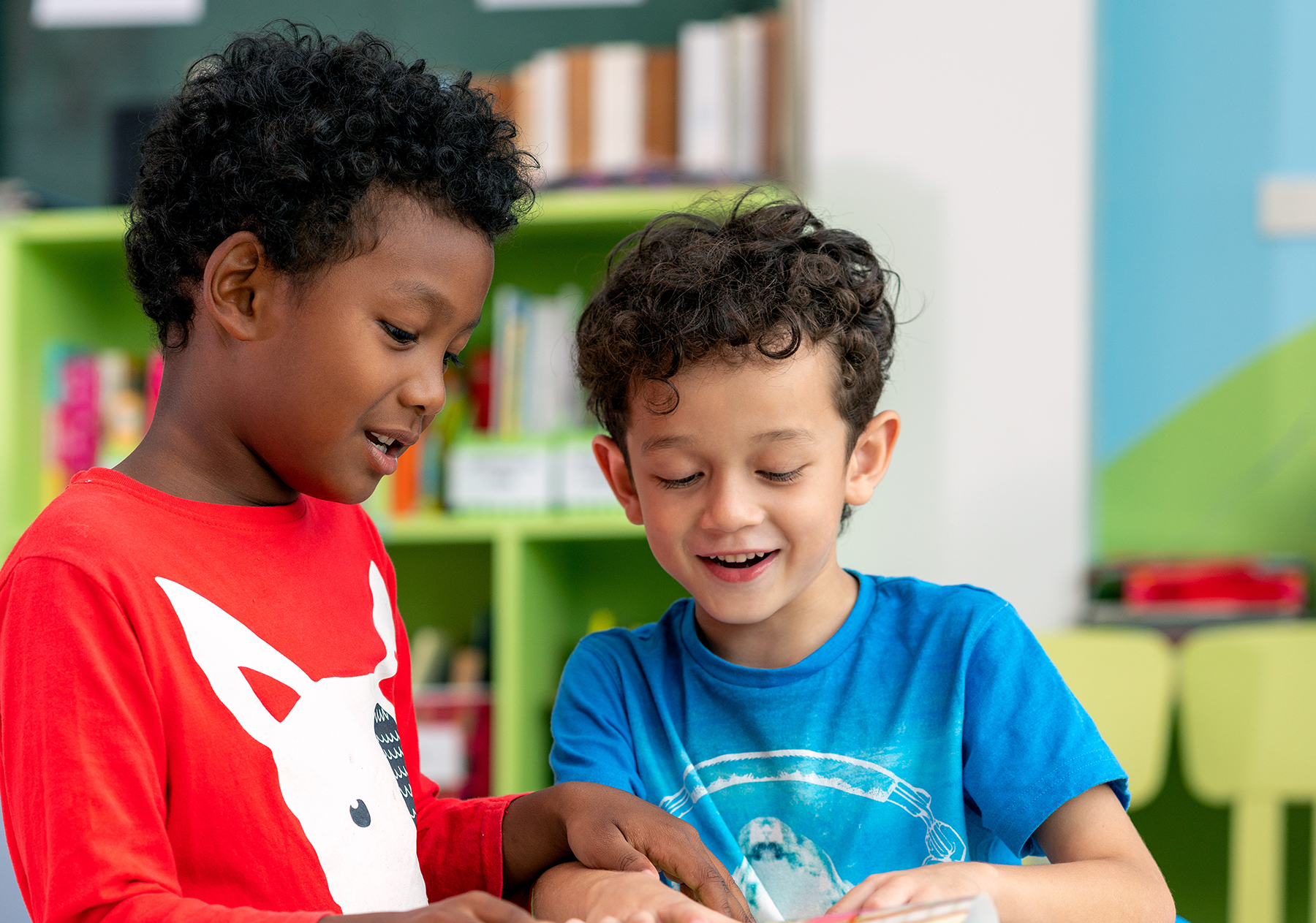 "Two young boys with dark curly hair smile while playing together"