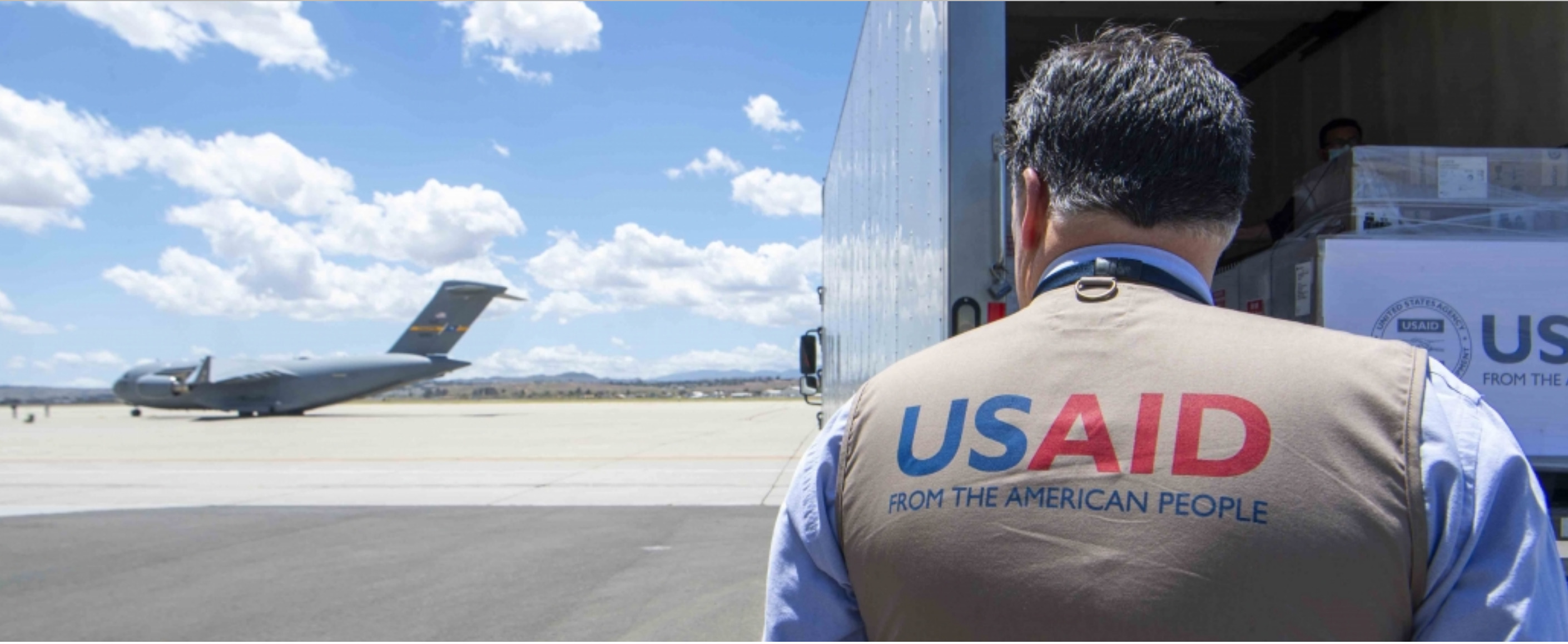 Worker wearing USAID vest, with plane in background