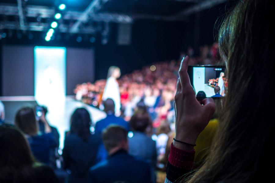 Woman holding camera recording fashion show with model on runway