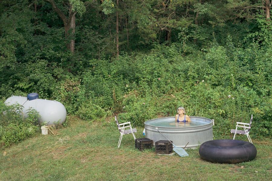 Woman wearing bathing suit and sunglasses, sitting in stock tank full of water.