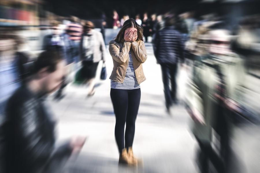 A woman buries her face in her hands while a busy crowd of people moves around her without interacting.