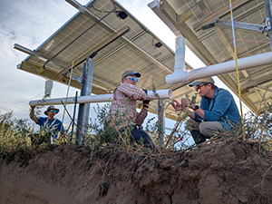 Three scientists install a solar recharge system in an unused corner of a Kansas crop field.