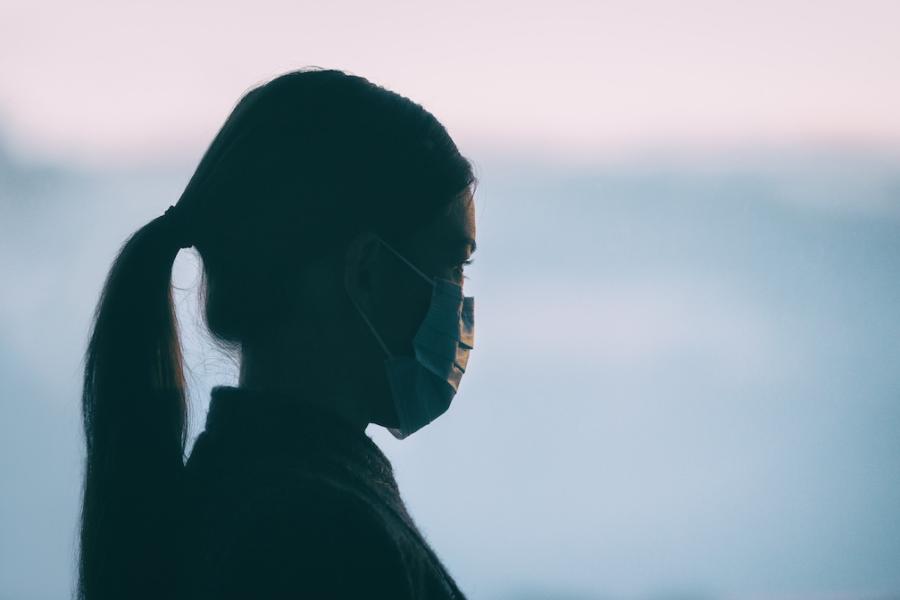 A young Asian woman wears a COVID mask while staring into the distance.