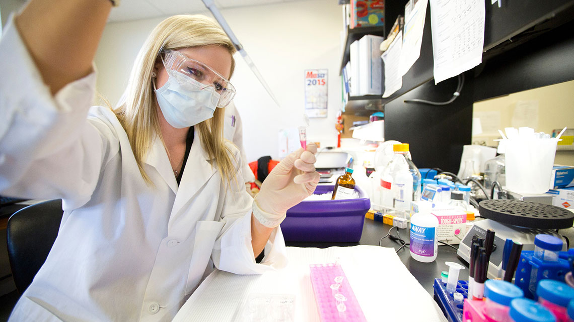 Masked student in lab coat works with sample in lab