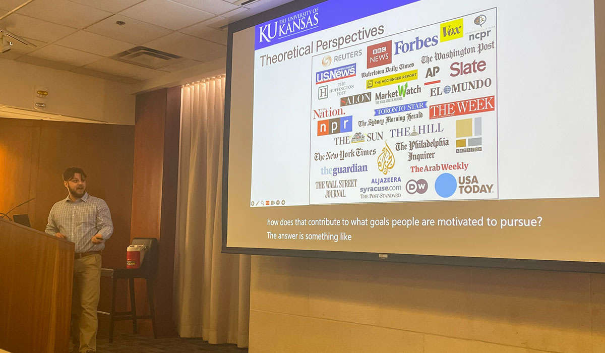 Logan Edmondson at podium with overhead presentation showing logos for companies for many media companies including AP, Slate, Marketwatch, NPR, The Nation and more.