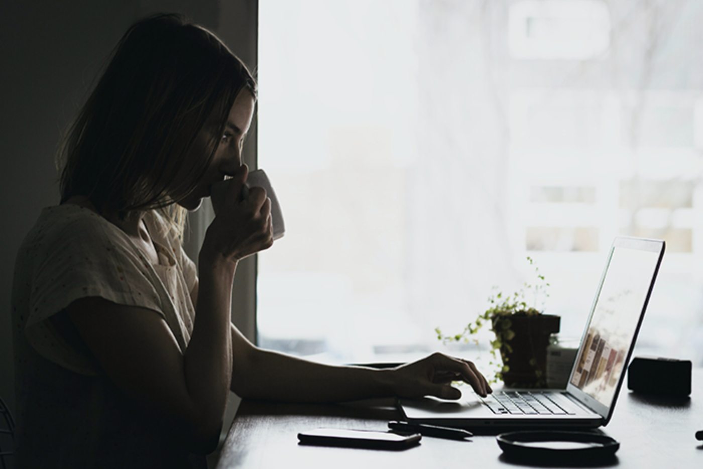 A woman sits and drinks coffee while looking at a laptop